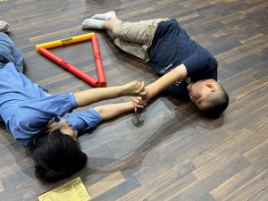 두명이서 누워서 서로 마주보고 팔을 뻗어 손잡는 사진